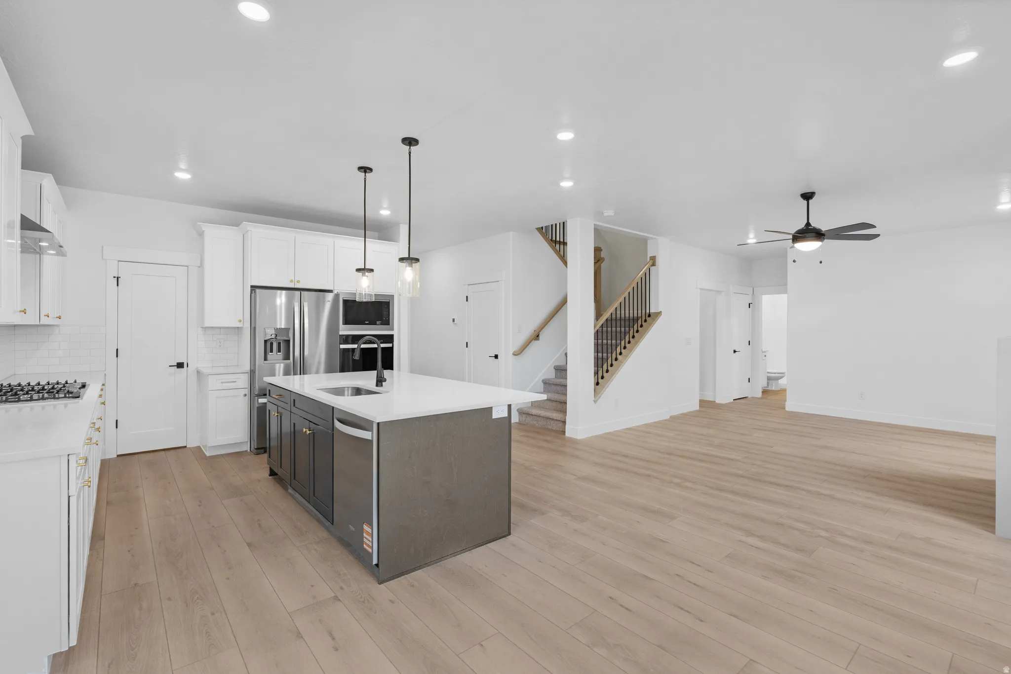 Two tone kitchen featuring two tone cabinets, pendant lighting, stainless steel appliances, light stone countertops, and light wood-type flooring