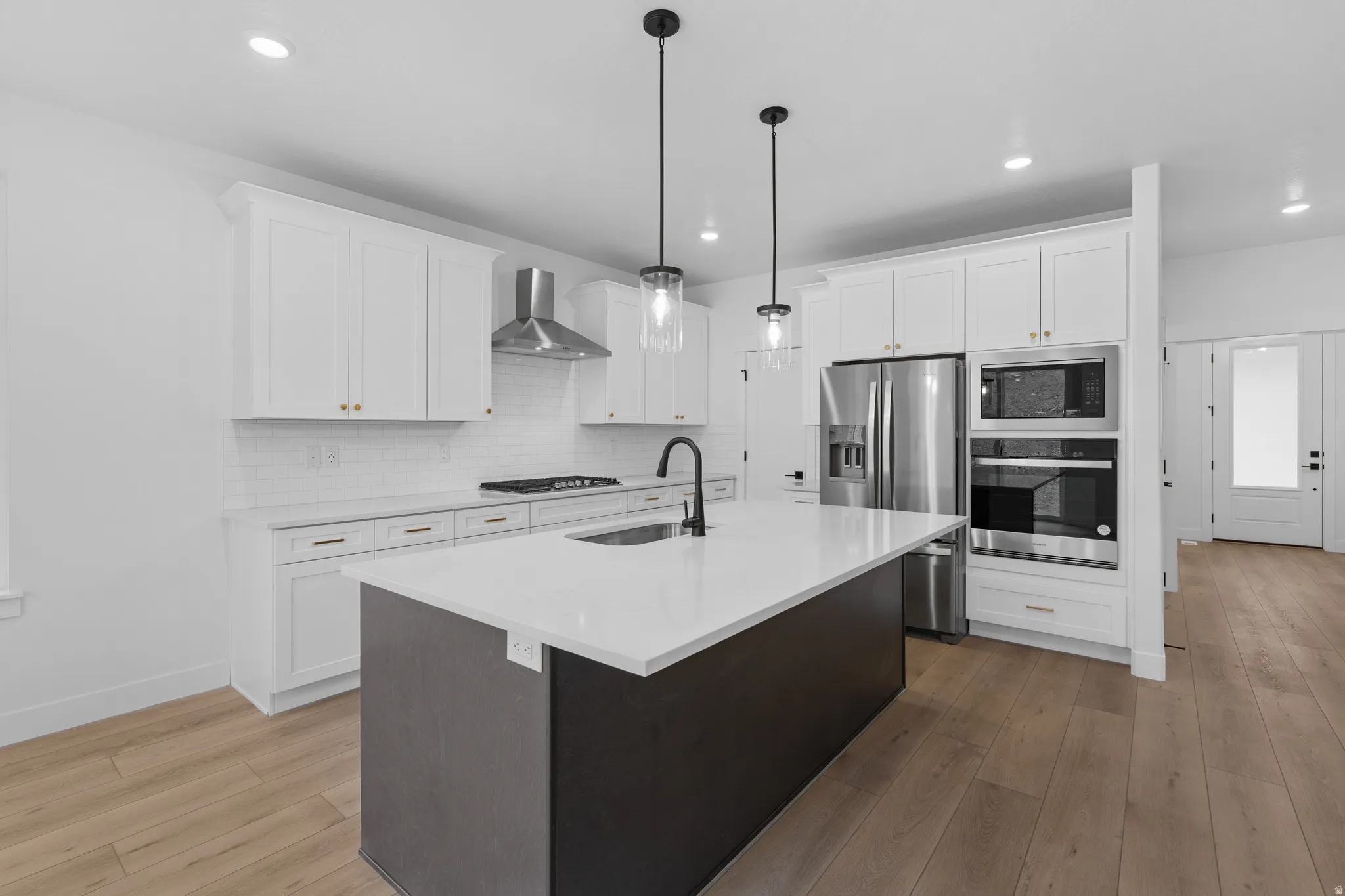 Two tone kitchen featuring dual tone cabinets, a kitchen island with sink, pendant lighting, stainless steel appliances, and light wood-style flooring