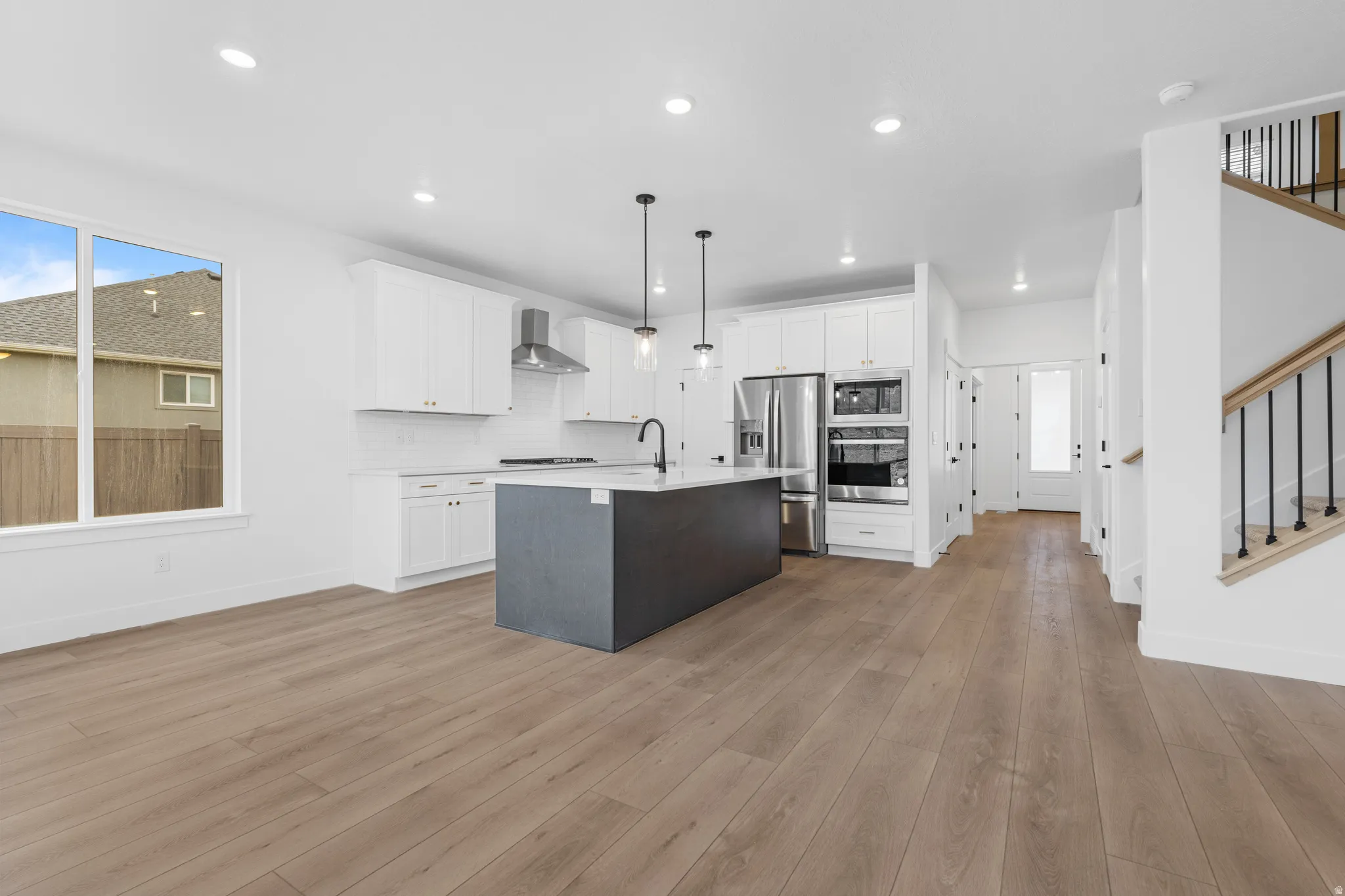 Two tone kitchen featuring two tone color scheme, stainless steel appliances, pendant lighting, a center island with sink, and light wood-style floors