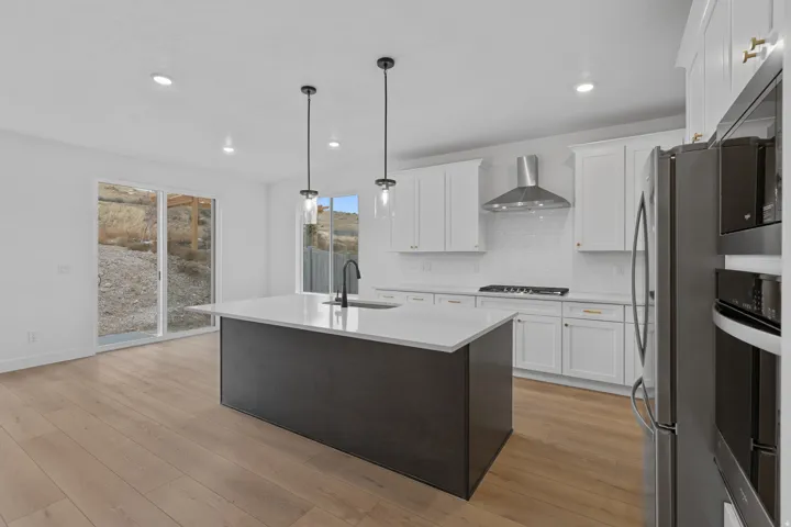 Kitchen featuring an island with sink, two tone cabinetry, stainless steel appliances, hanging light fixtures, and decorative backsplash