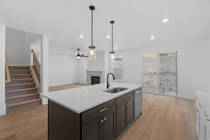 Dual tone kitchen with a fireplace, hanging light fixtures, a center island with sink, light wood-type flooring, and light stone counters