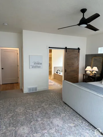 Bedroom with a barn door, ensuite bathroom, a ceiling fan, carpet, and a textured ceiling