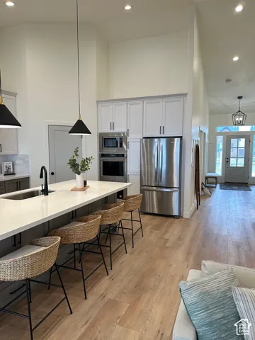 Two tone kitchen featuring decorative light fixtures, a kitchen breakfast bar, stainless steel appliances, a high ceiling, and light wood finished floors