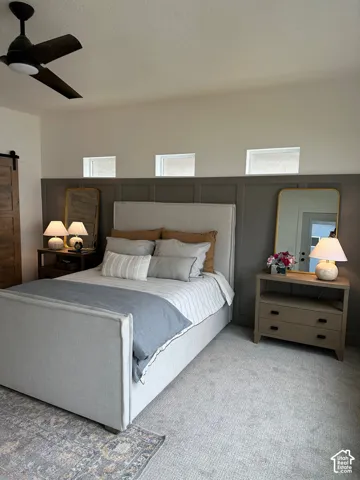 Bedroom with a barn door, carpet floors, and a ceiling fan