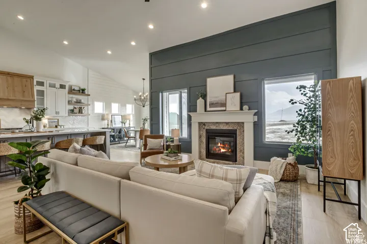 Living room featuring light wood-type flooring, vaulted ceiling, suspended lighting, and a glass covered fireplace