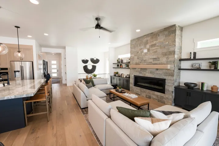 Living room with light wood-style flooring, a stone fireplace, a ceiling fan, and recessed lighting