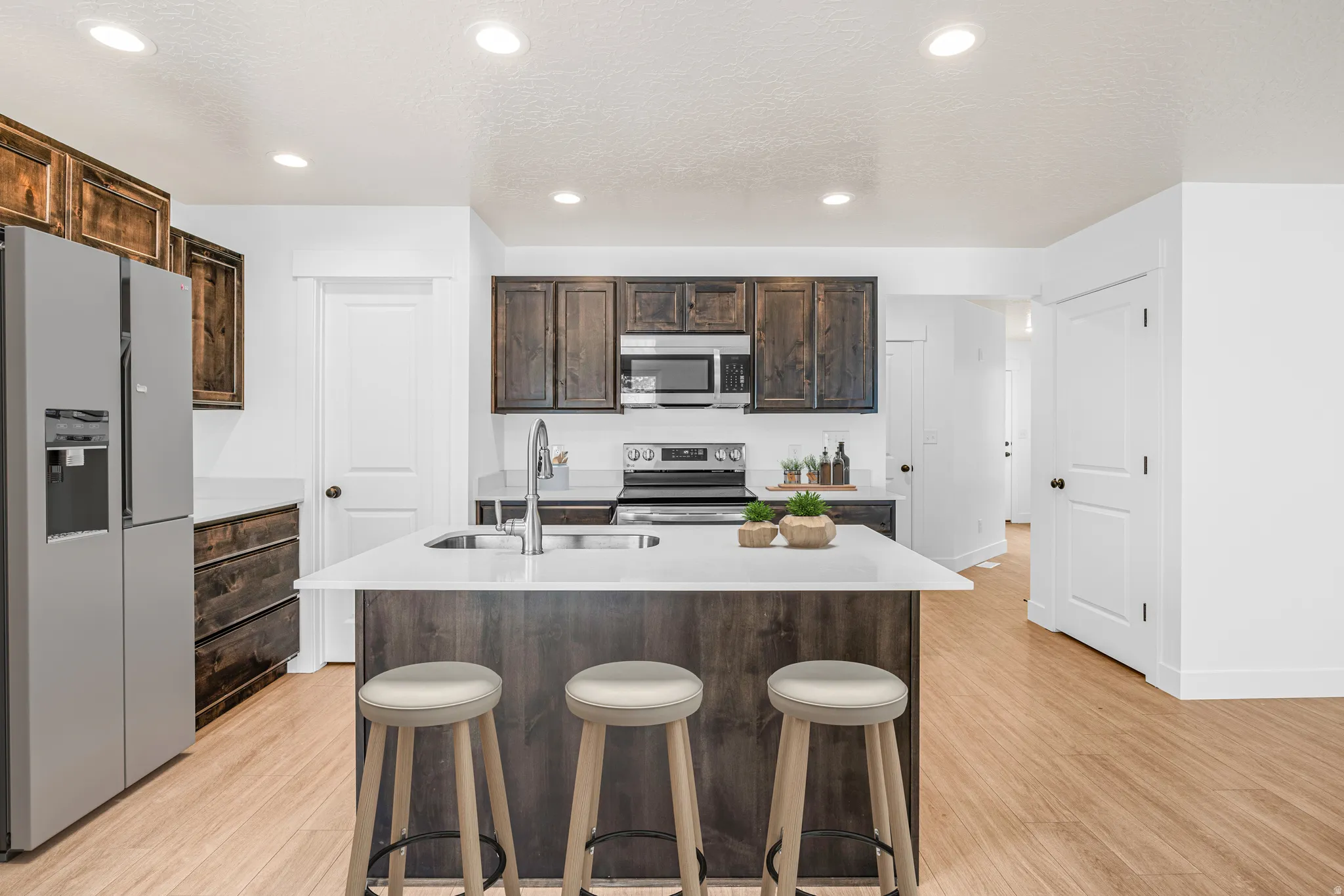 Kitchen with dark wood finish cabinets, stainless steel appliances, a kitchen breakfast bar, light wood-type flooring, and an island with sink