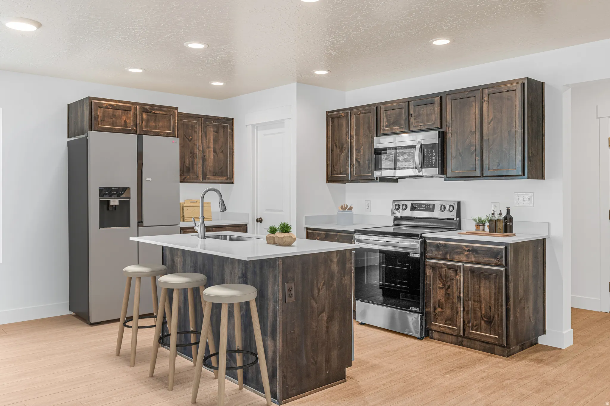 Kitchen with dark wood finish cabinets, stainless steel appliances, a kitchen breakfast bar, a textured ceiling, and a kitchen island with sink