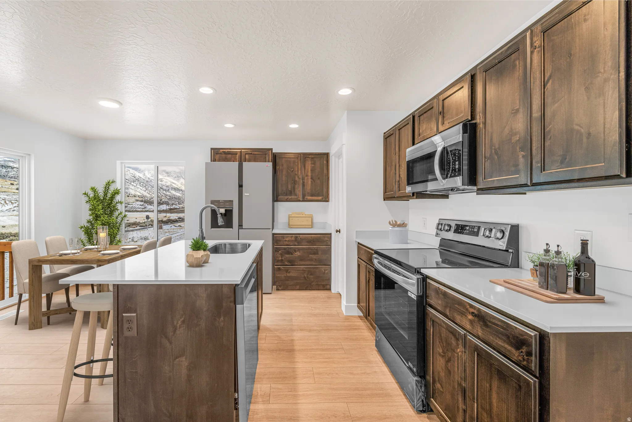 Kitchen with dark wood finish cabinets, stainless steel appliances, a kitchen island with sink, a textured ceiling, and recessed lighting