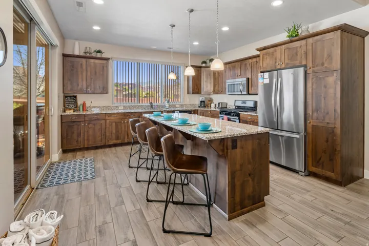 Kitchen featuring stainless steel appliances, light stone counters, hanging light fixtures, a kitchen island, and wood tiled floors