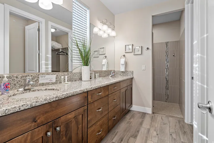 Primary Bathroom with double vanity, a tile shower, and wood finish floors