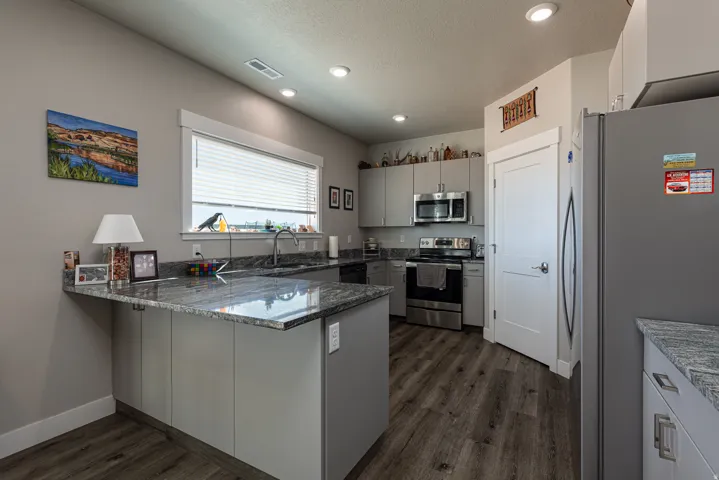 Kitchen featuring stainless steel appliances, a peninsula, dark stone countertops, dark wood-style floors, and recessed lighting