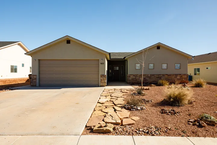 Ranch-style home with stucco siding, driveway, an attached garage, and stone siding