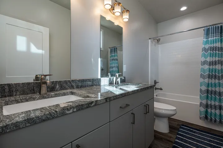 Bathroom with double vanity, dark wood-type flooring, shower / bath combination with curtain, and recessed lighting