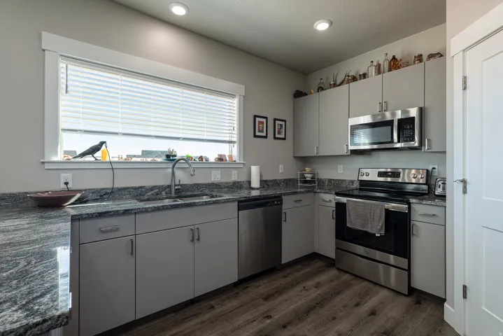 Kitchen featuring stainless steel appliances, gray cabinetry, dark wood-style flooring, dark stone countertops, and recessed lighting