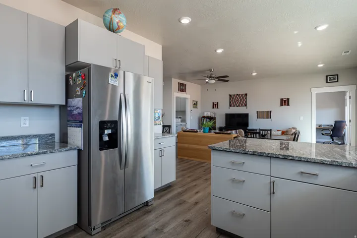 Kitchen with stainless steel fridge, light stone countertops, open floor plan, ceiling fan, and dark wood-type flooring