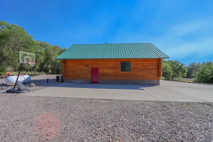 Log cabin exterior with a green metal roof, a single window, and a red entry door, complemented by a concrete pad