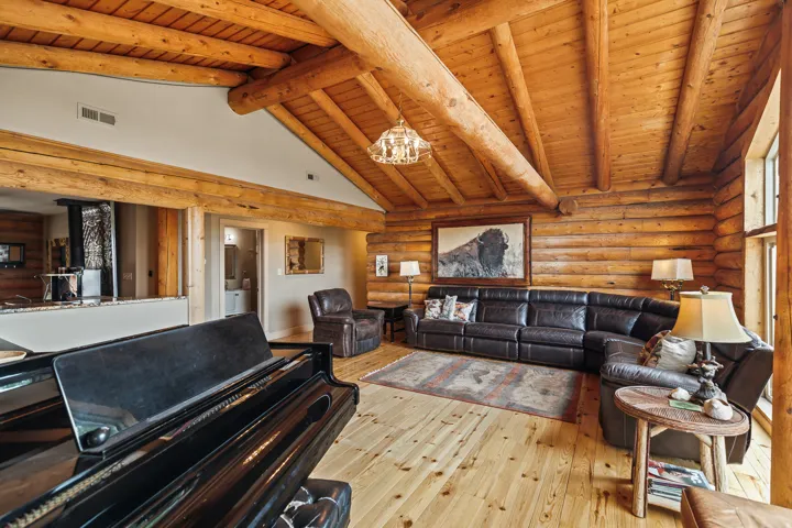 Living room with log walls, light wood finished floors, a high wood beamed ceiling, and hanging lights