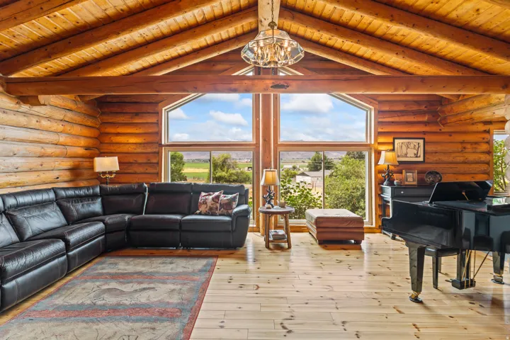 Living room with rustic walls, a wood ceiling with exposed beams, light wood-style flooring, and hanging lights