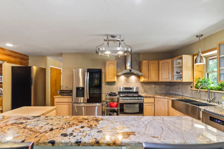 Kitchen featuring stainless steel appliances, light stone counters, tasteful backsplash, open shelves, and light wood finish cabinets