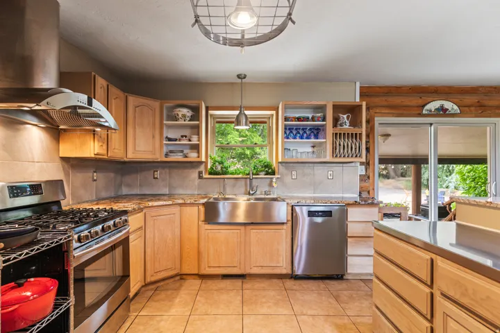 Kitchen with stainless steel appliances, pendant lighting, light tile patterned flooring, open shelves, and backsplash