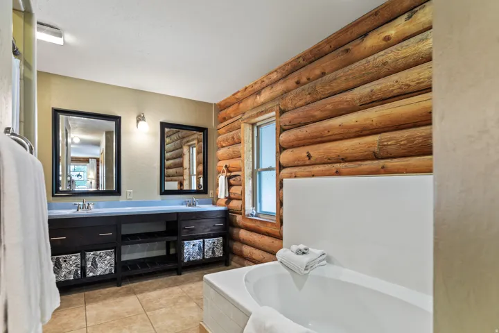 Bathroom featuring log walls, double vanity, light tile patterned flooring, and a bath