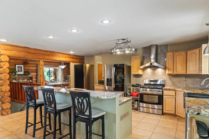 Kitchen featuring stainless steel appliances, log walls, light stone countertops, a center island, and a breakfast bar