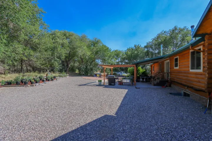 Expansive gravel patio area with a wooden pergola and mature trees bordering the property