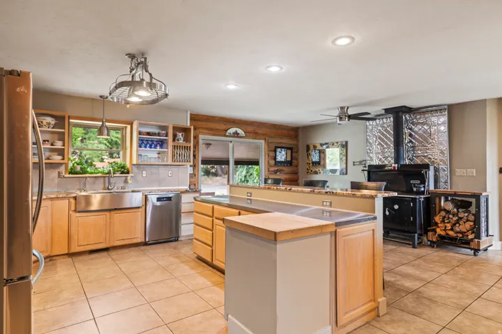 Kitchen with open shelves, light wood finish cabinetry, stainless steel appliances, light tile patterned floors, and rustic walls