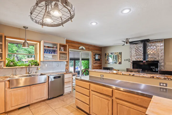 Kitchen with dishwasher, hanging light fixtures, stainless steel countertops, tasteful backsplash, and light tile patterned floors