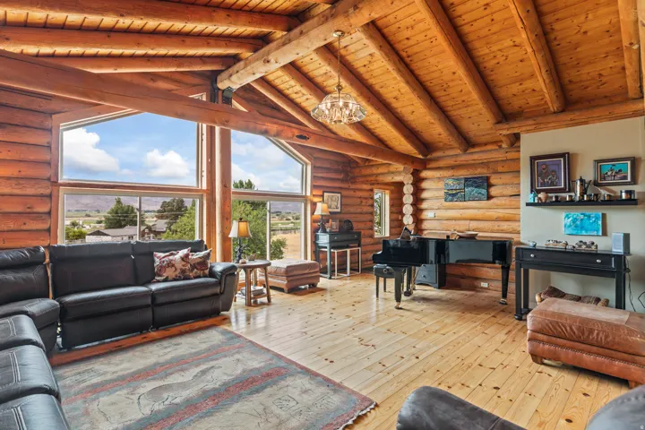 Living room with rustic walls, a high wood beamed ceiling, light wood-style floors, and suspended lighting