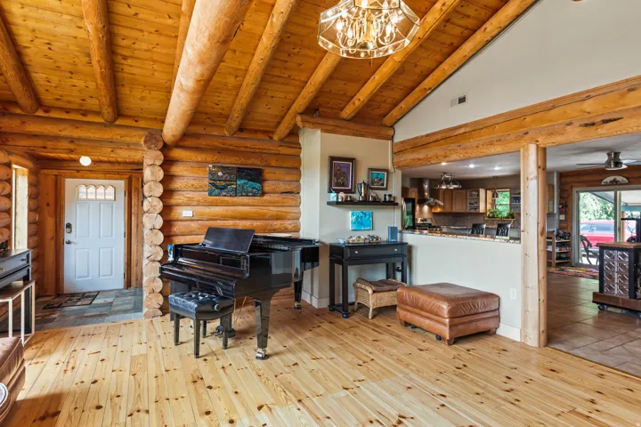 Living room featuring log walls, hardwood / wood-style floors, a high wooden beamed ceiling, suspended lighting, and ceiling fan