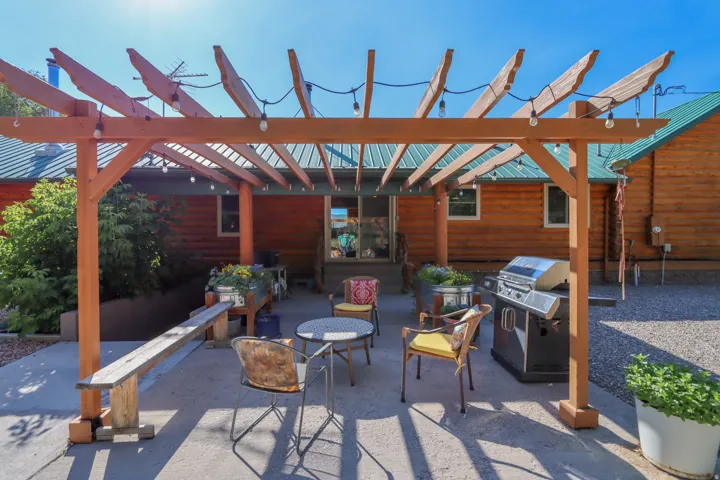 Outdoor patio featuring a wood pergola with string lighting, concrete flooring, and a gravel area