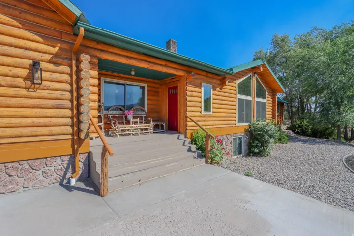 Log cabin exterior featuring a covered porch with a red entry door, stone foundation accents, and a concrete walkway