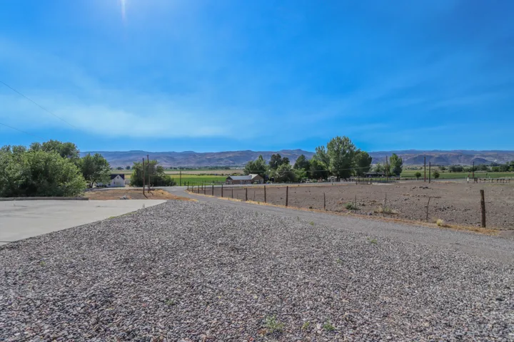 Gravel driveway extending towards distant green fields and mountains under a clear sky