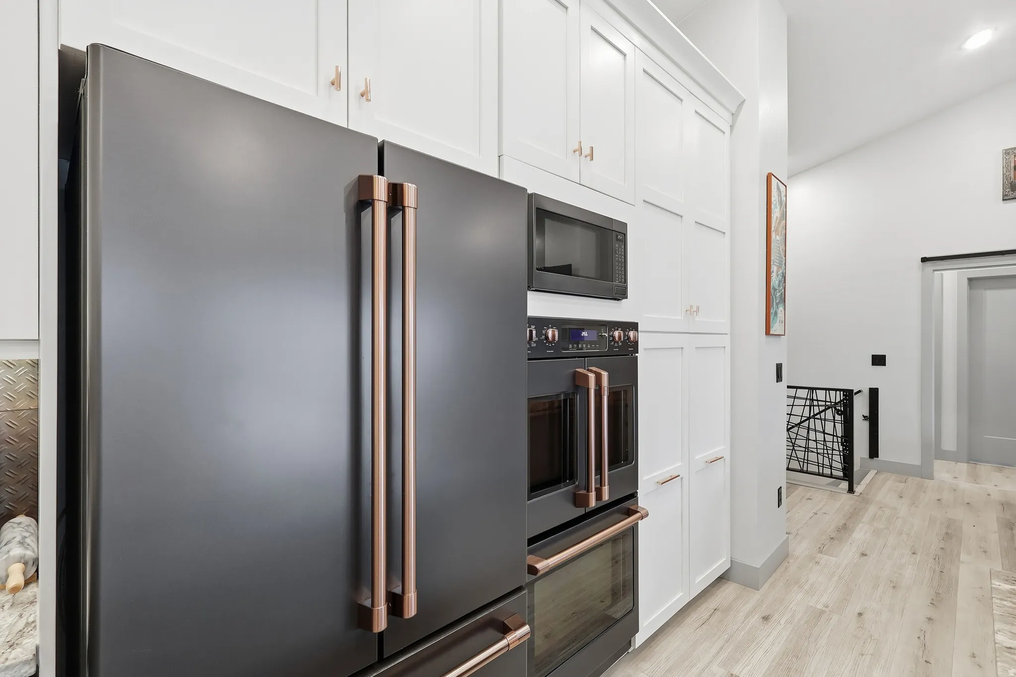Kitchen with black appliances, white cabinetry, double oven, light wood-type flooring, recessed lighting, and lofted ceiling