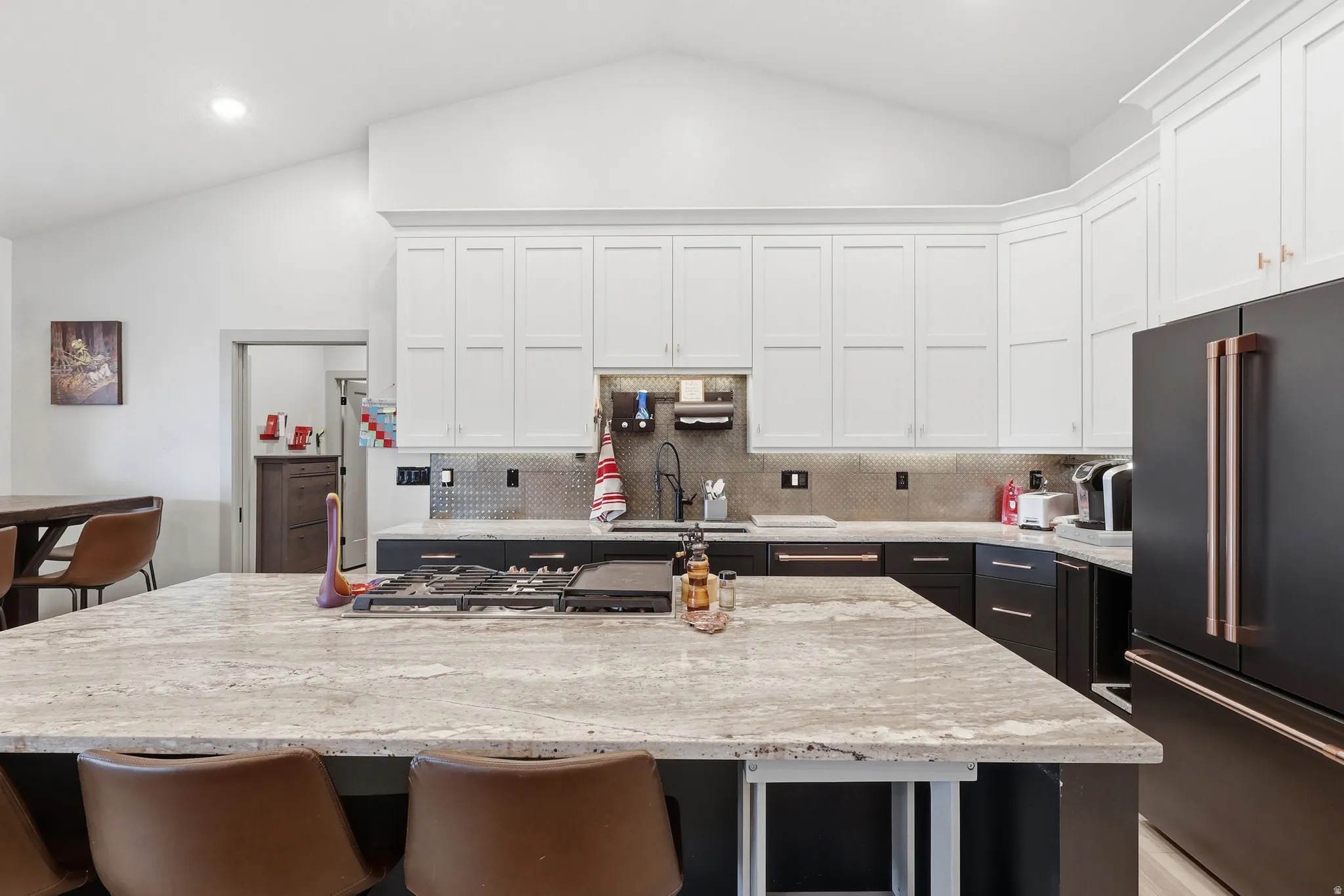 Kitchen with high quality fridge, a breakfast bar, a center island, light stone counters, and vaulted ceiling
