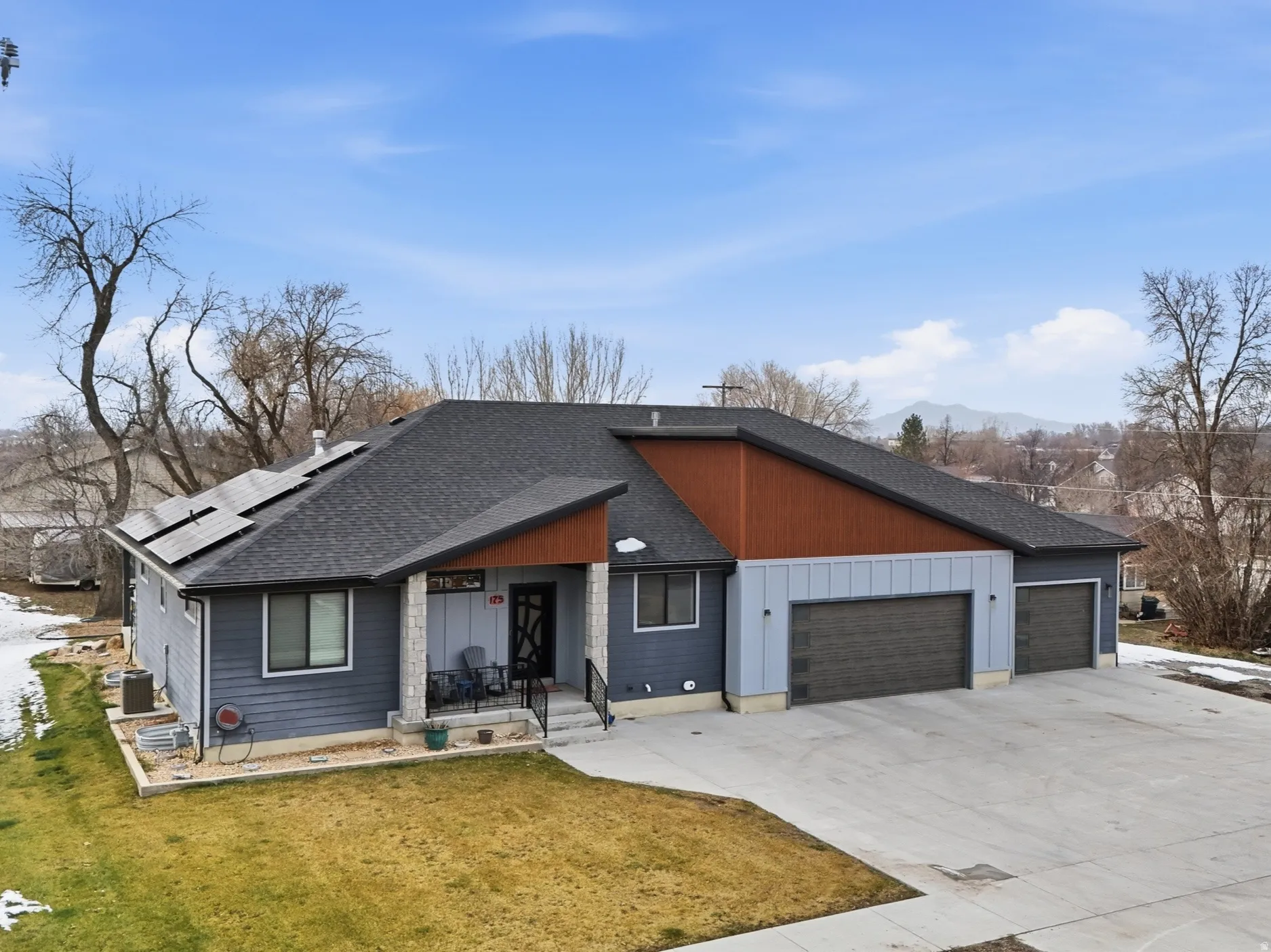 View of front of home featuring roof with shingles, an attached garage, driveway, roof mounted solar panels, and a front yard