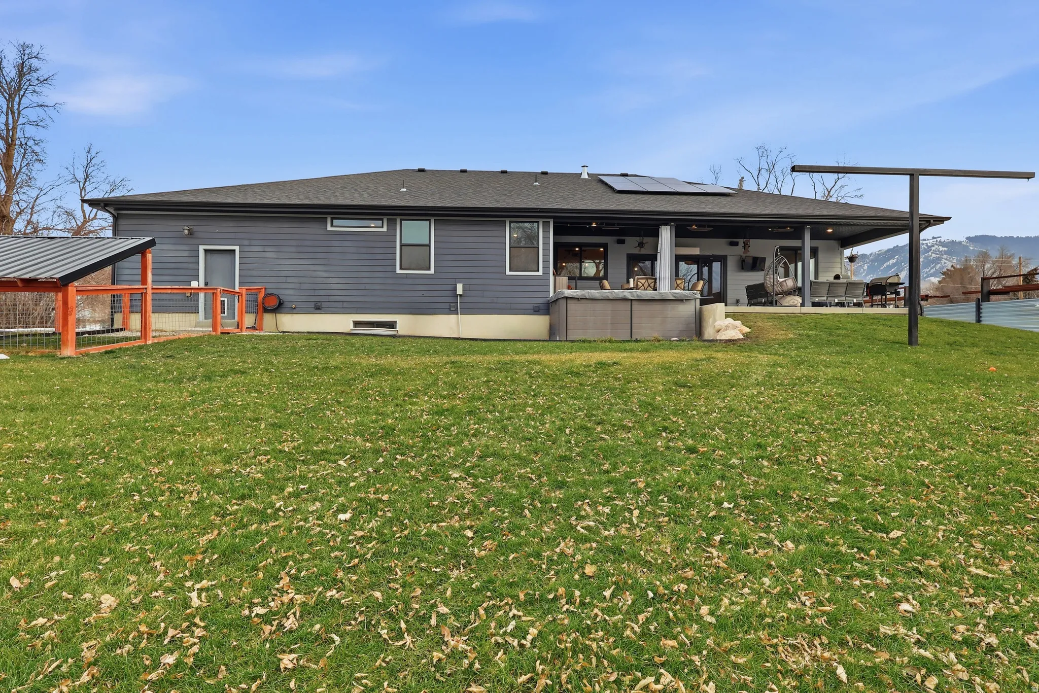 Rear view of house featuring roof mounted solar panels, a shingled roof, a covered heated deck, a swim spa and a yard