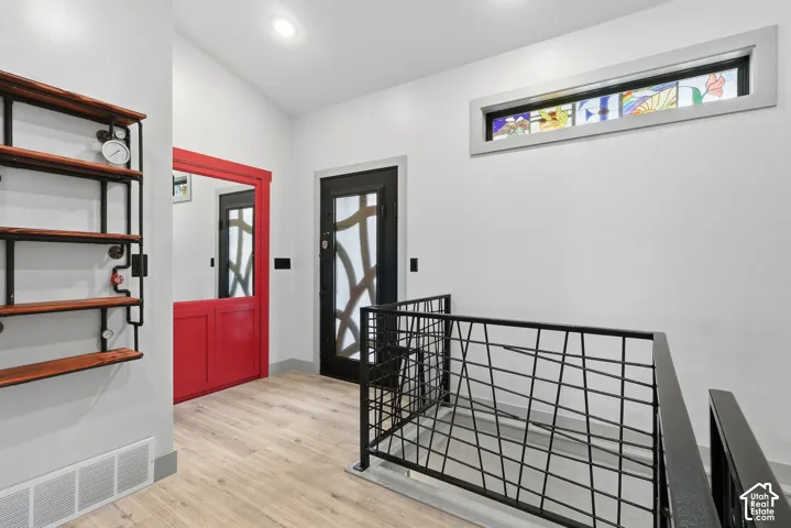 Entrance foyer with light wood-type flooring, custom metal railing, a hidden door and vaulted ceiling