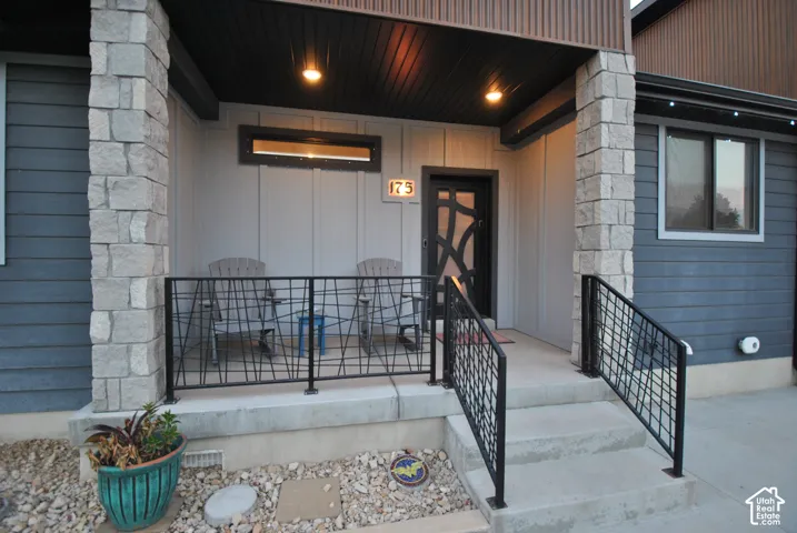 Covered entry porch featuring stone-clad columns, black metal railings, and a modern front door with decorative glass