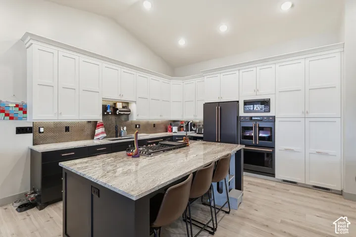 Kitchen featuring vaulted ceiling, double wall oven, light stone counters, a center island, and a breakfast bar