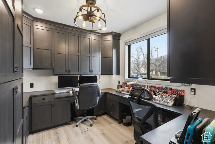 Office with built in desk, light wood-style flooring, and suspended lighting