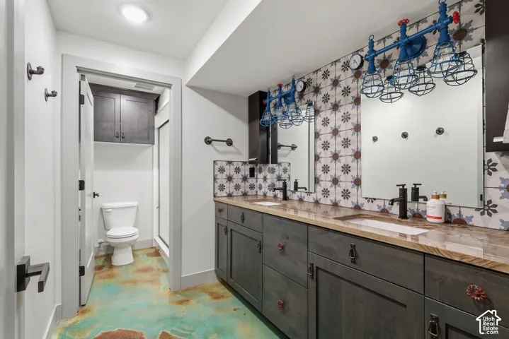 Bathroom with double vanity, backsplash, concrete flooring, and a shower stall