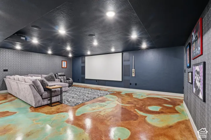 Home theater featuring wallpapered walls, finished concrete flooring, and a textured ceiling
