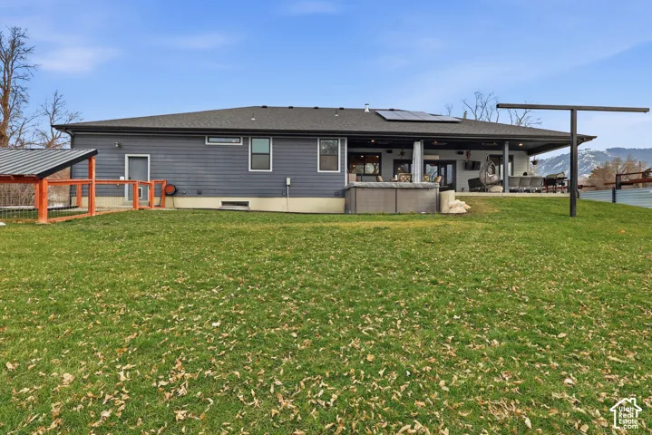 Rear view of house featuring roof mounted solar panels, a shingled roof, a covered heated deck, a swim spa and a yard