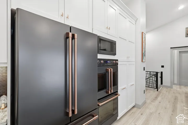 Kitchen with black appliances, white cabinetry, double oven, light wood-type flooring, recessed lighting, and lofted ceiling
