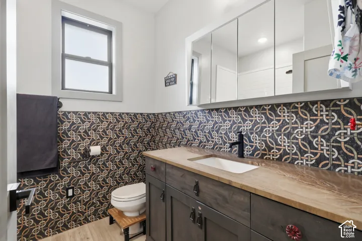 Full bathroom featuring vanity, light wood-style flooring, a wainscoted wall, and tile walls