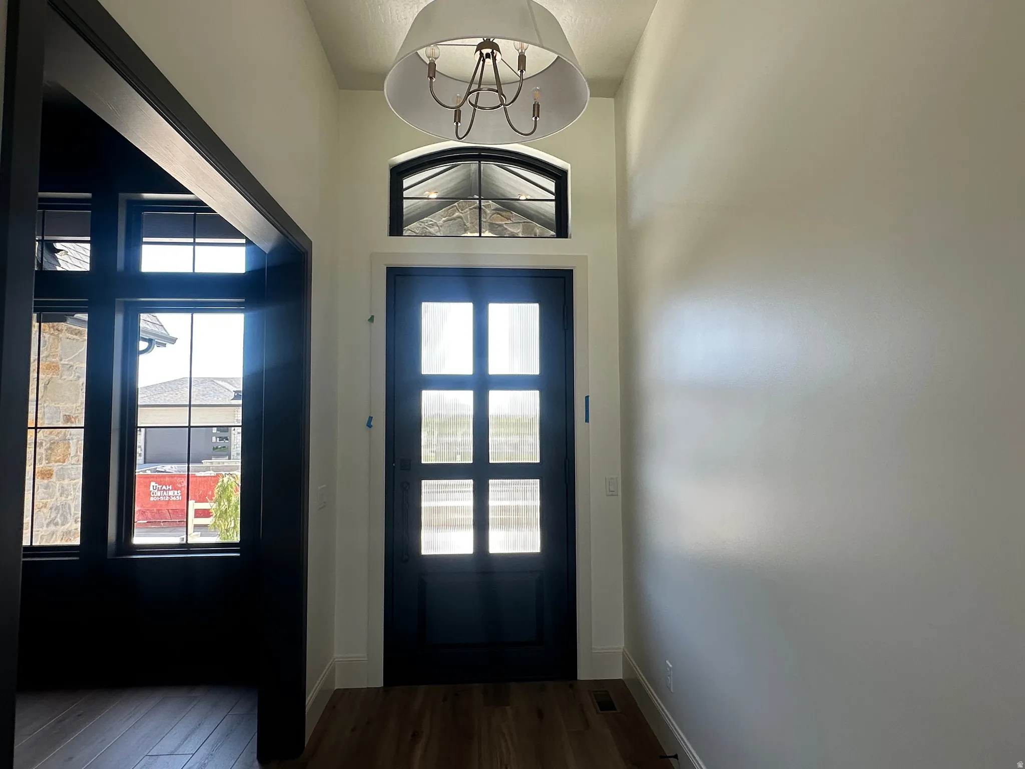 Entryway featuring a dark paneled door with glass inserts, an arched transom window, and a drum pendant light fixture