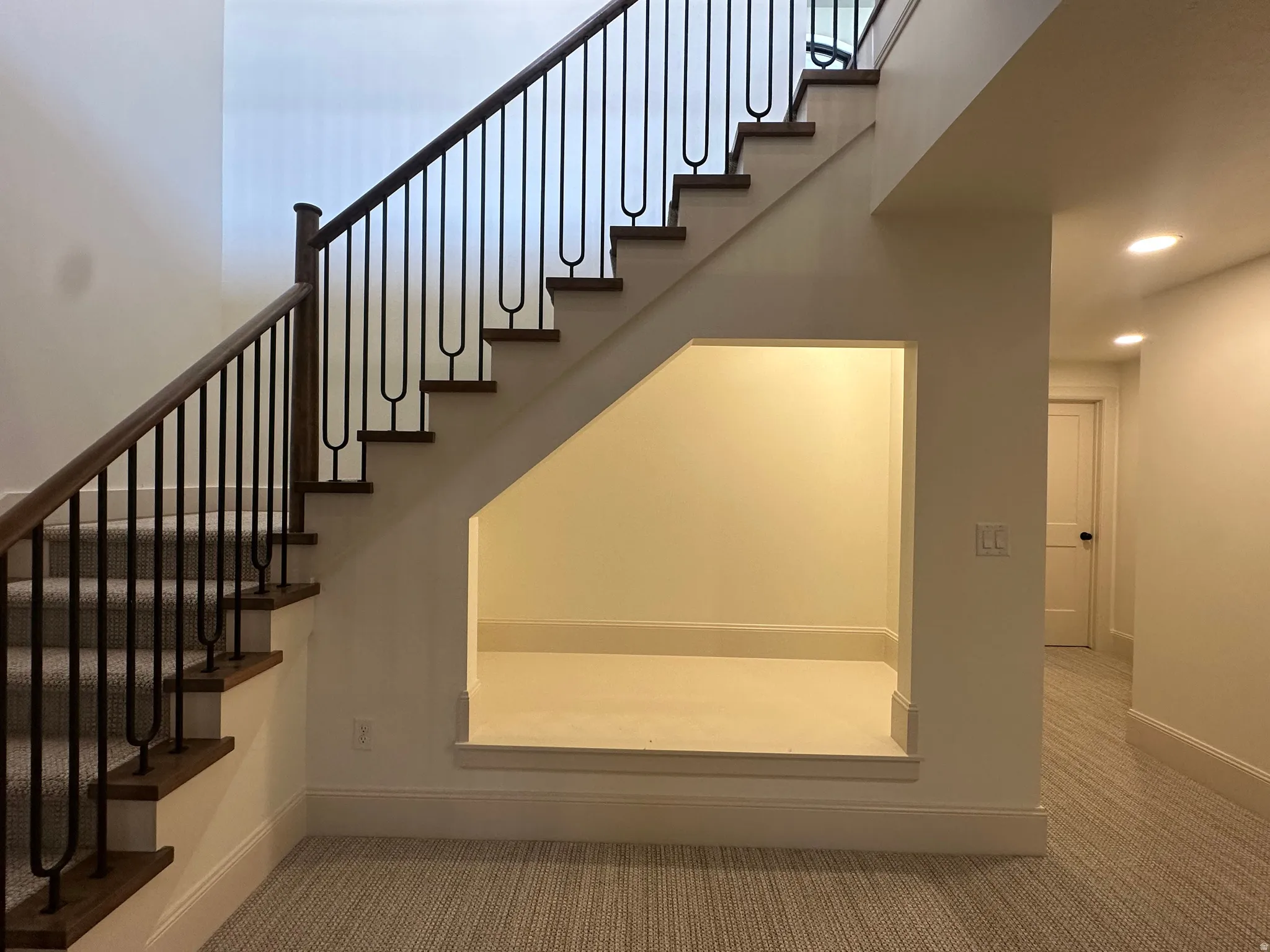 Book nook under staircase. Staircase featuring dark wood handrails, black metal balusters, and carpeted treads